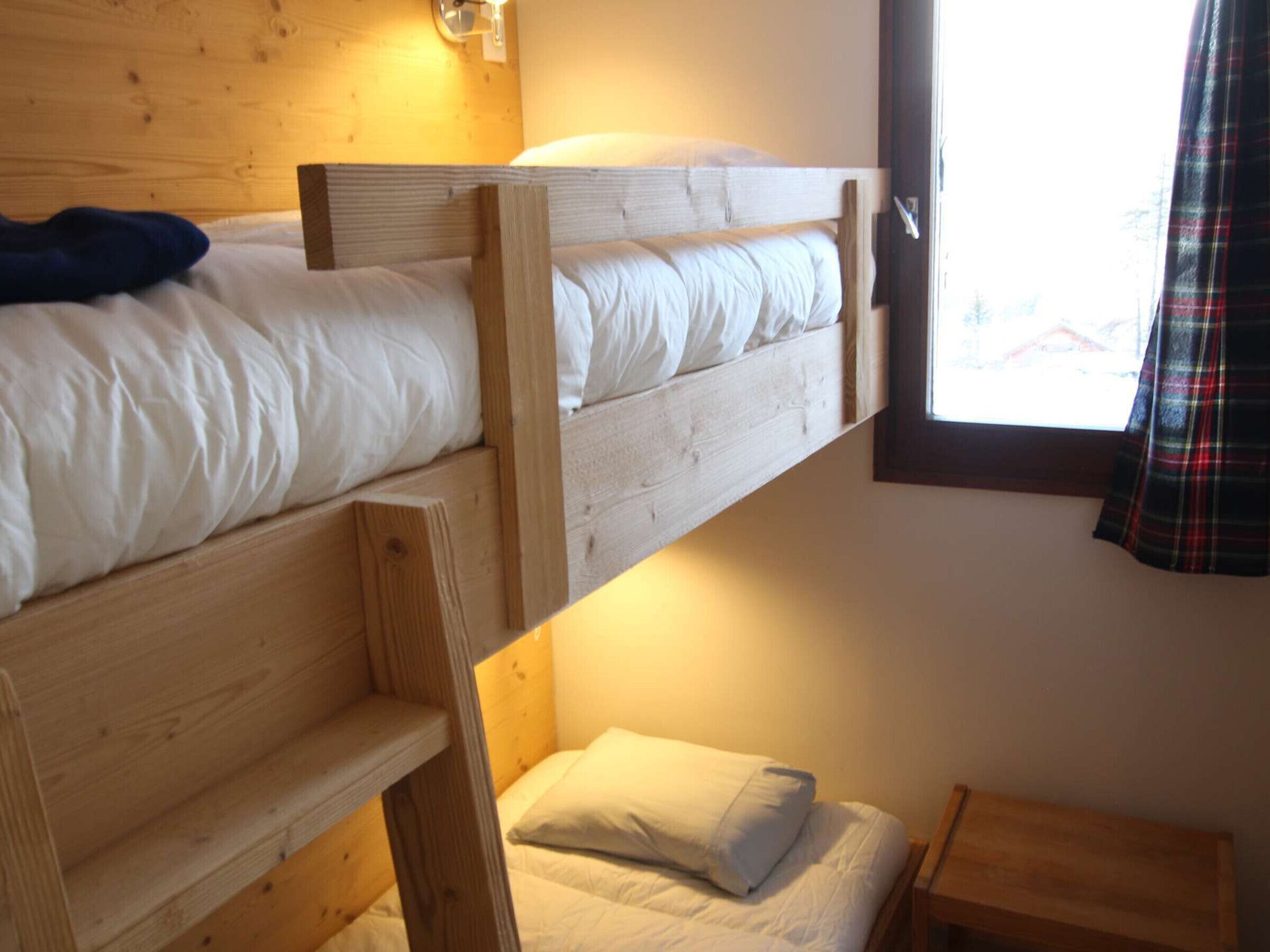 Een slaapkamer met stapelbedden, houten hoofdeinden, een klein nachtkastje en een raam met uitzicht.