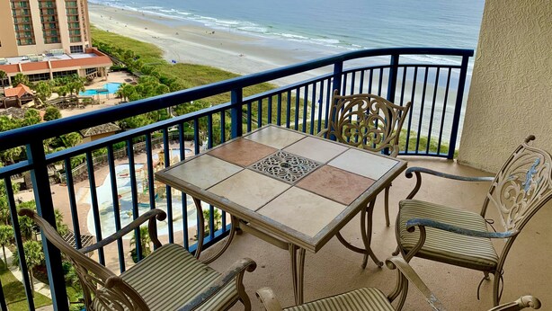 Un balcon avec une table et des chaises donnant sur une plage et l’océan.