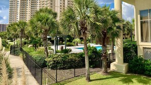 Un immeuble de grande hauteur doté de nombreux balcons, entouré de palmiers et d’un jardin bien entretenu.