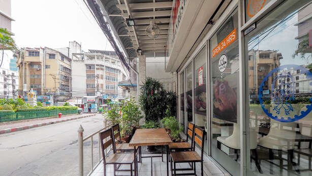 An outdoor seating area with a wooden table and chairs, a small garden, and a sign indicating the establishment is open 24 hours. - OYO 75362 Swagath Home (Bangkok)
