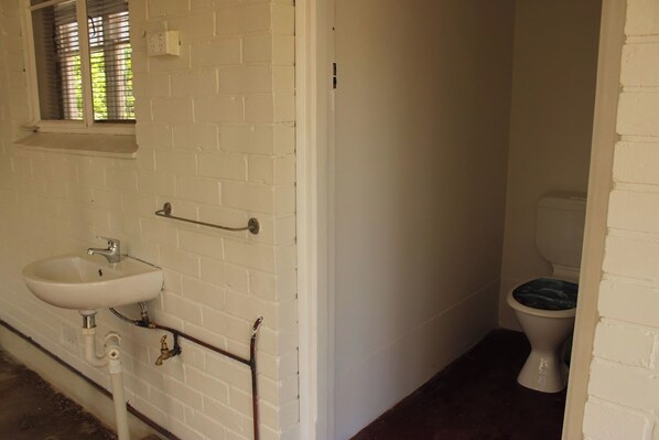 Een kleine badkamer met witte wanden, een wastafel, een toilet en een raam met zonwering.