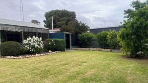 A grassy yard with a building, a large tree, and a metal fence. - Paradise @ Port Hughes, 500M walk to beach, ALL LINEN & TOWELS PROVIDED (Port Hughes)