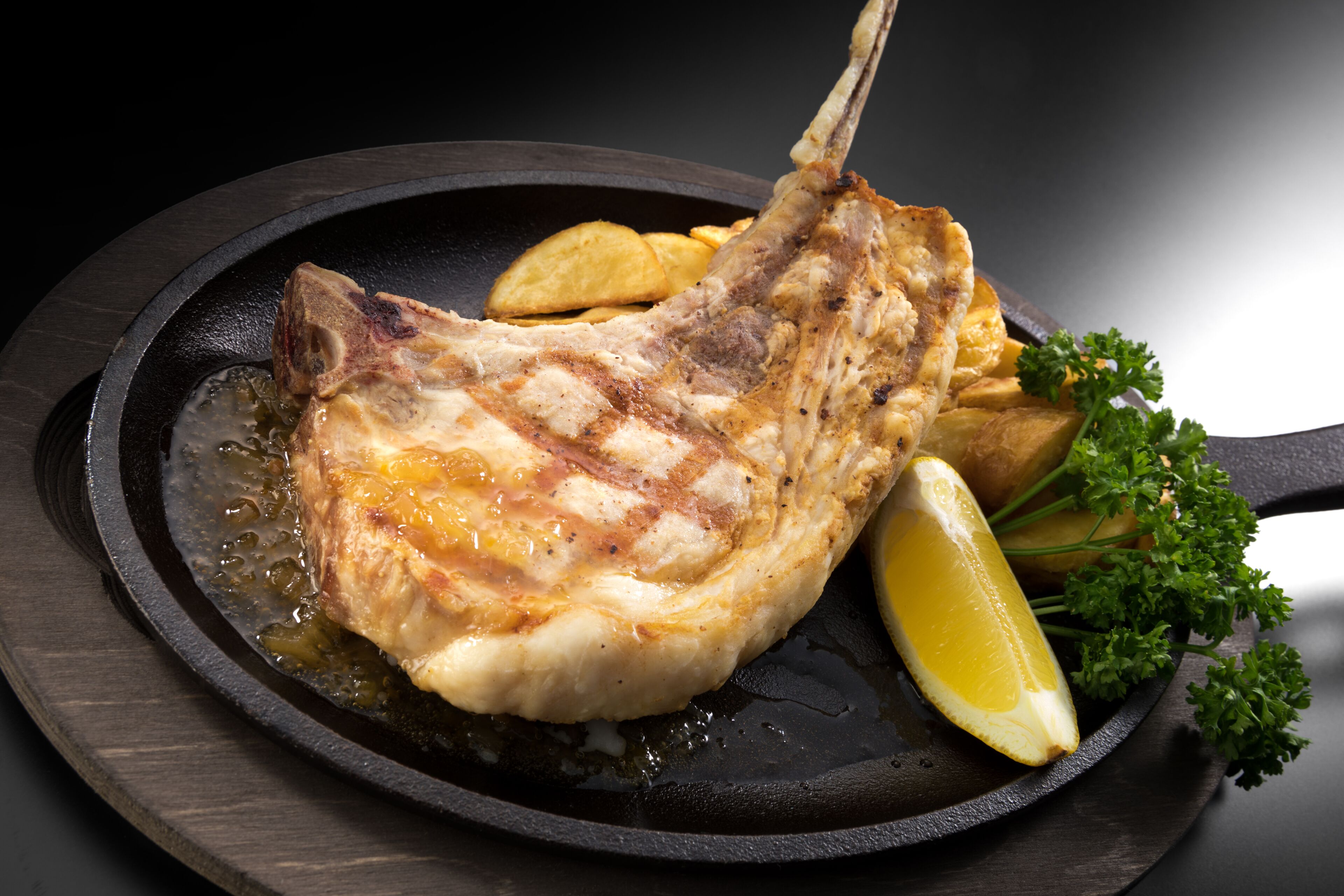 A grilled fish fillet with lemon and potatoes on a black skillet.