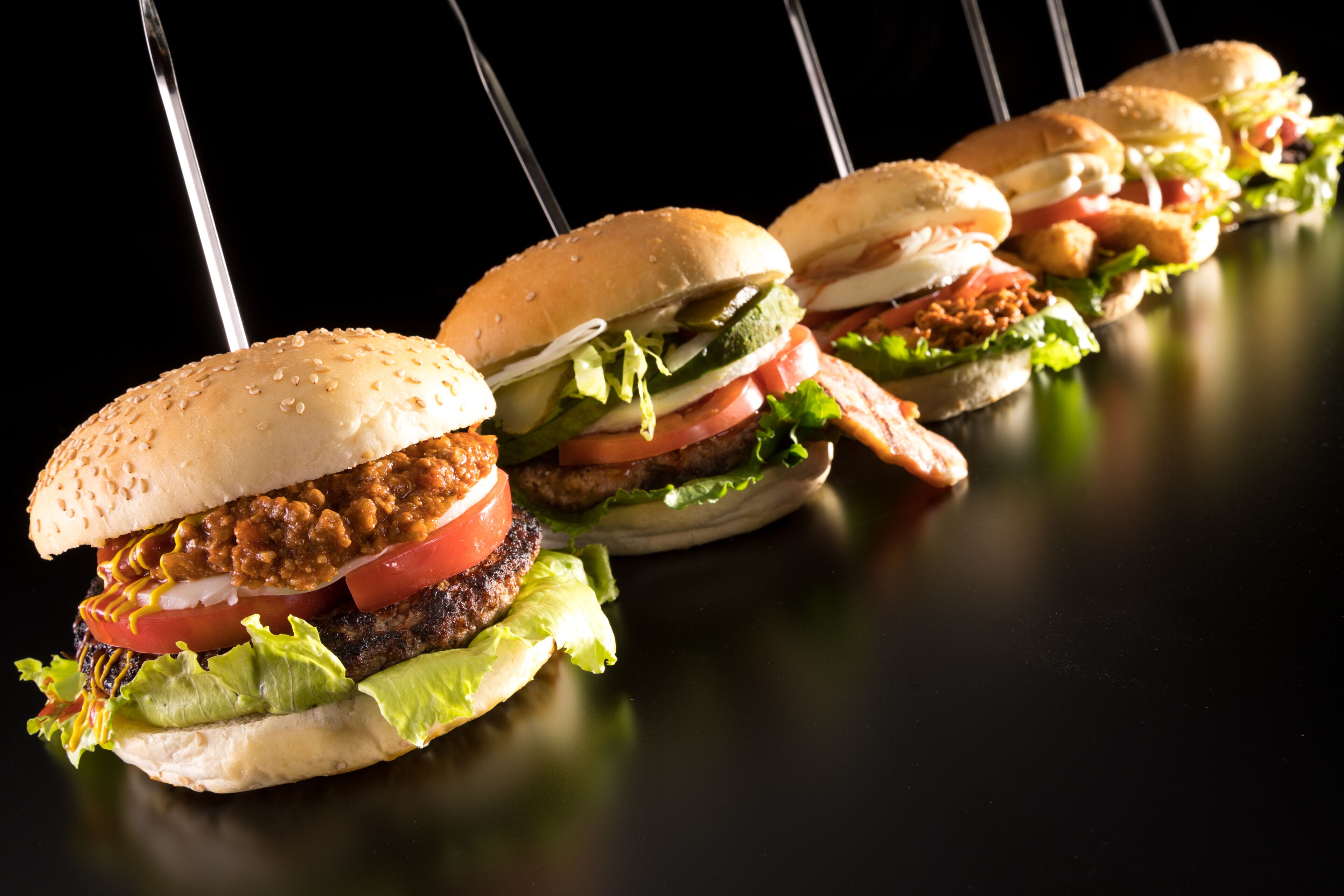 Una fila di hamburger su una superficie nera con sfondo scuro.