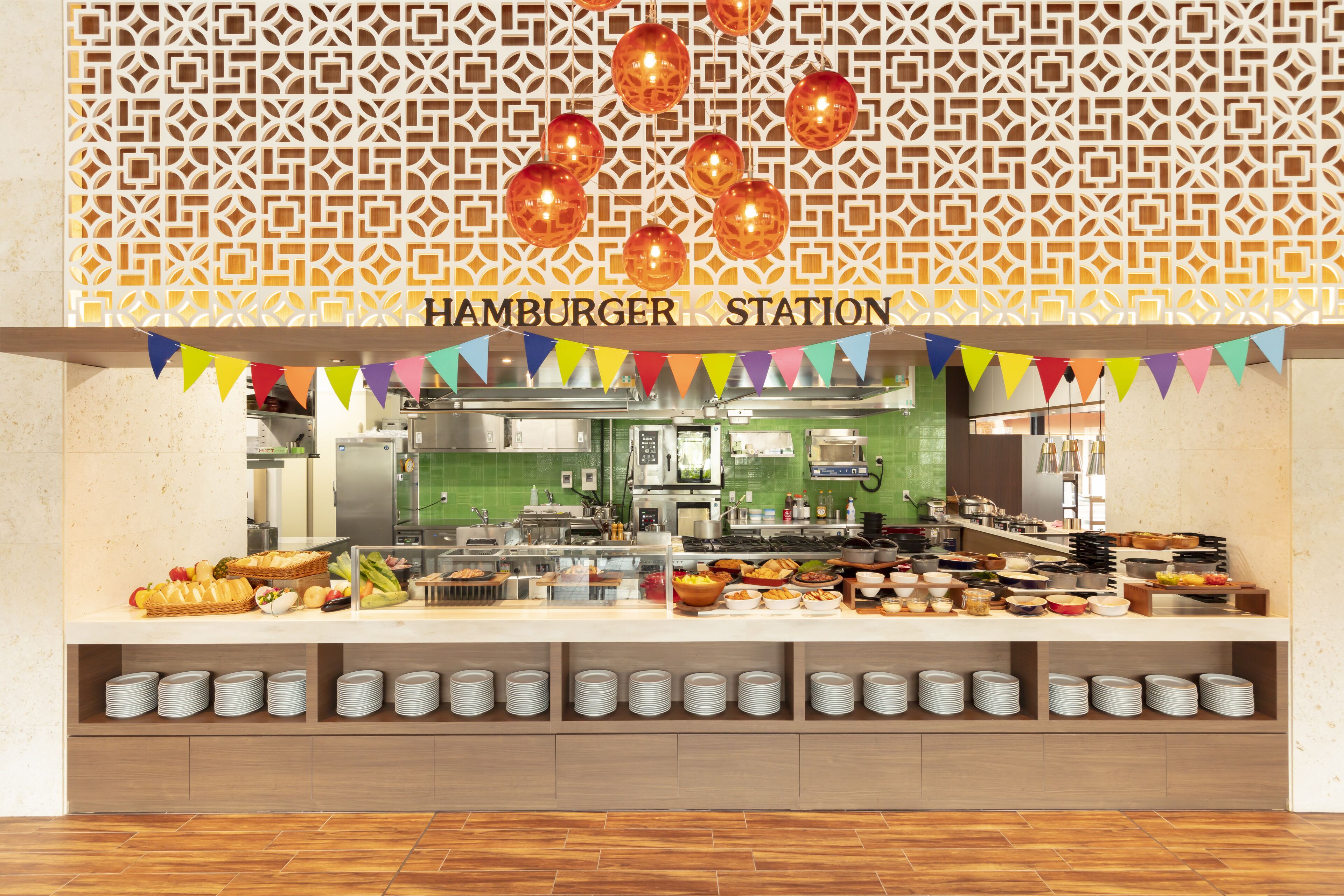 A buffet area with a variety of food items, a kitchen in the background, and a decorative wall with geometric patterns.