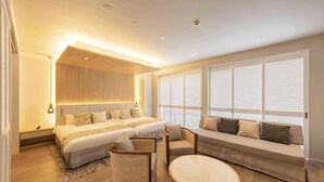 Una habitación de hotel moderna con una cama grande, un sofá, una mesita y un área de estar con vistas al exterior a través de amplios ventanales.