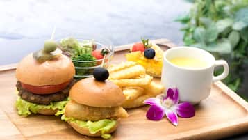 Une planche en bois sur laquelle sont disposés un hamburger, des frites, une salade et une tasse de café.