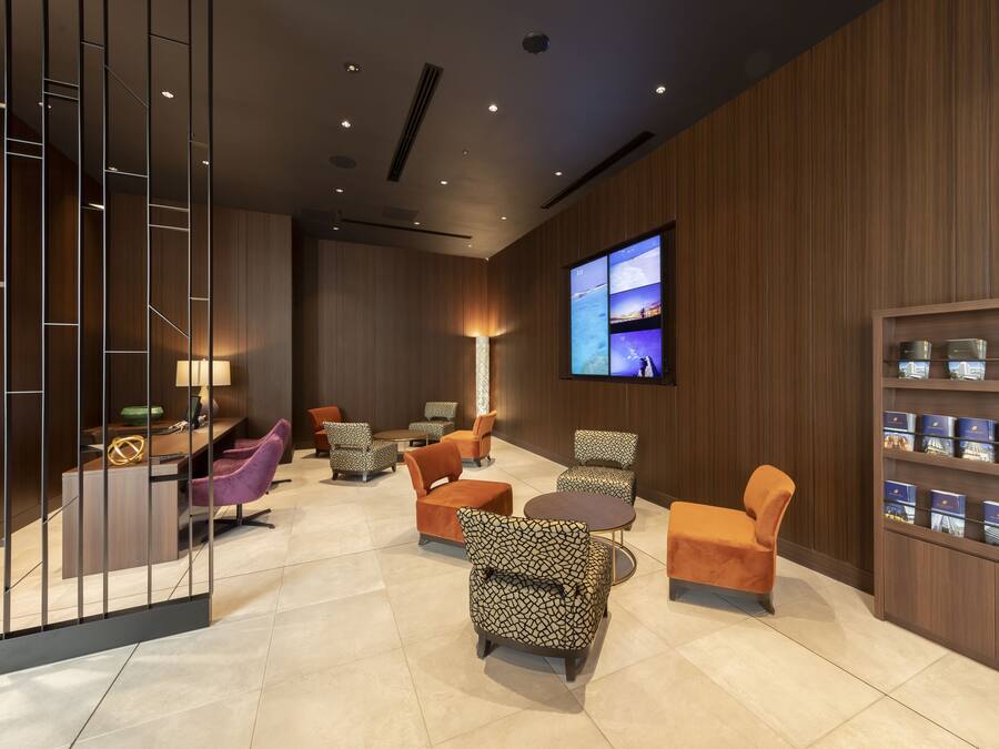 A modern lobby with wooden paneling, a TV mounted on the wall, and a variety of seating options including patterned and solid-colored chairs.