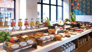 Montaje tipo bufé con diversos alimentos y bebidas, dispuesto en una larga mesa con vista a la calle.