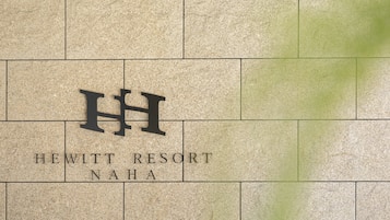 Pared de azulejos con el texto "HEWITT RESORT NAHA" y un gran logotipo en forma de "H".