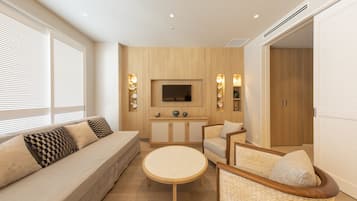 A modern living room with a sofa, armchairs, a round coffee table, and a TV mounted on the wall.