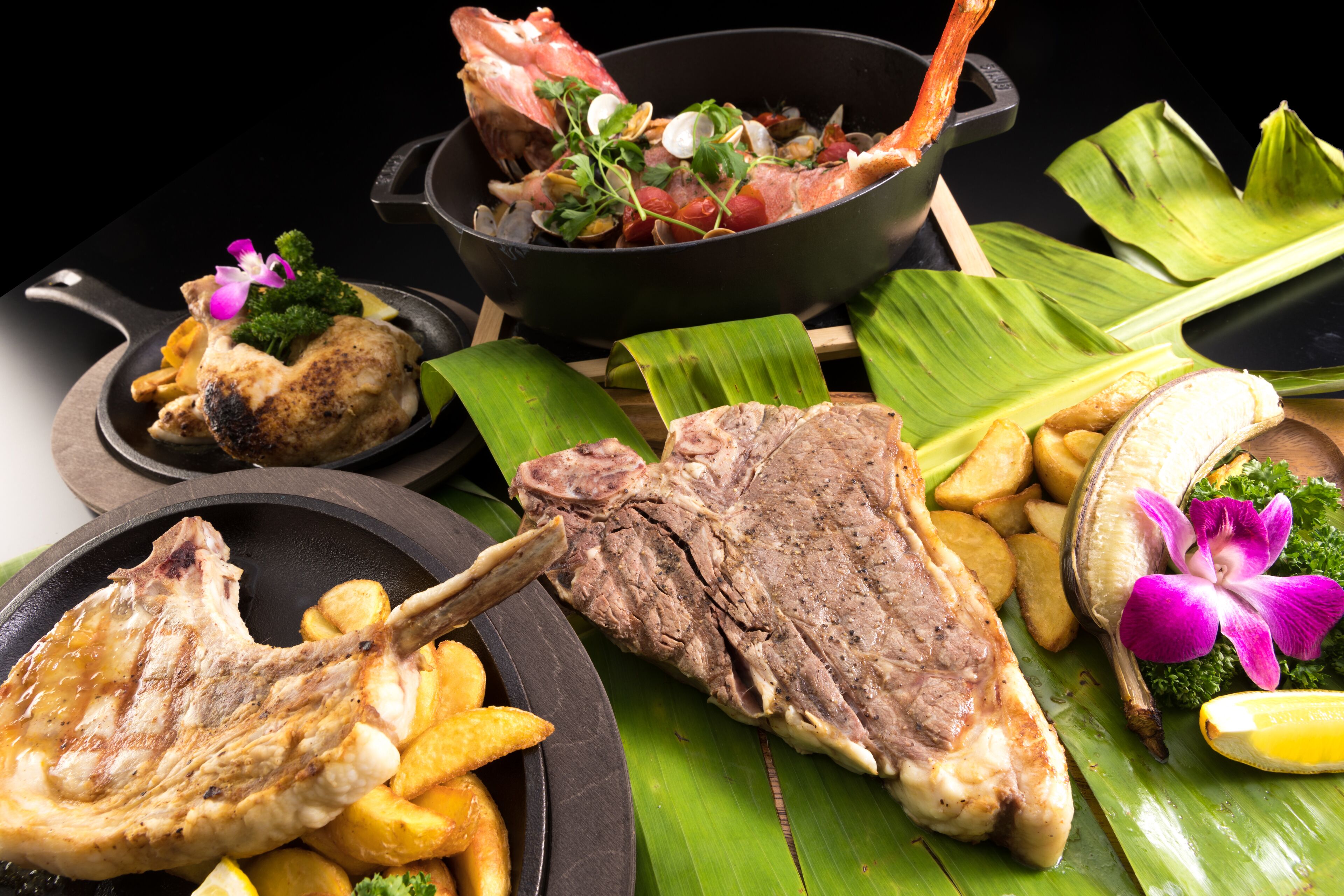 A variety of dishes including grilled meat, fries, and seafood, arranged on a table with a black background.