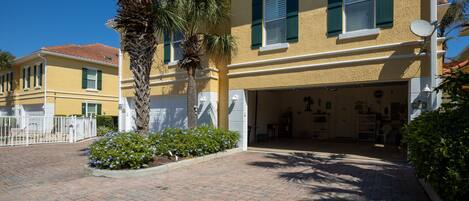 A yellow building with green shutters, a paved driveway, and a palm tree.