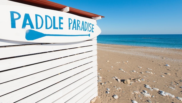 Een bord aan het strand met de tekst 'Paddle Paradise' en een paddle symbool.