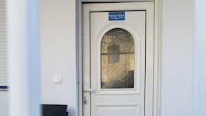 Een witte deur met een bordje 'Sunny Beach', een ruit en een welkomstmat.