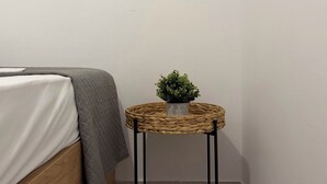 Een hoekzaak met een bed, een ronde geweven spiegel, een klein rond tafeltje met een plant en een houten kast.