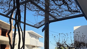 Een gebouw aan de kust met een balkon dat uitkijkt over de zee, een geparkeerde auto en een boom met kale takken.