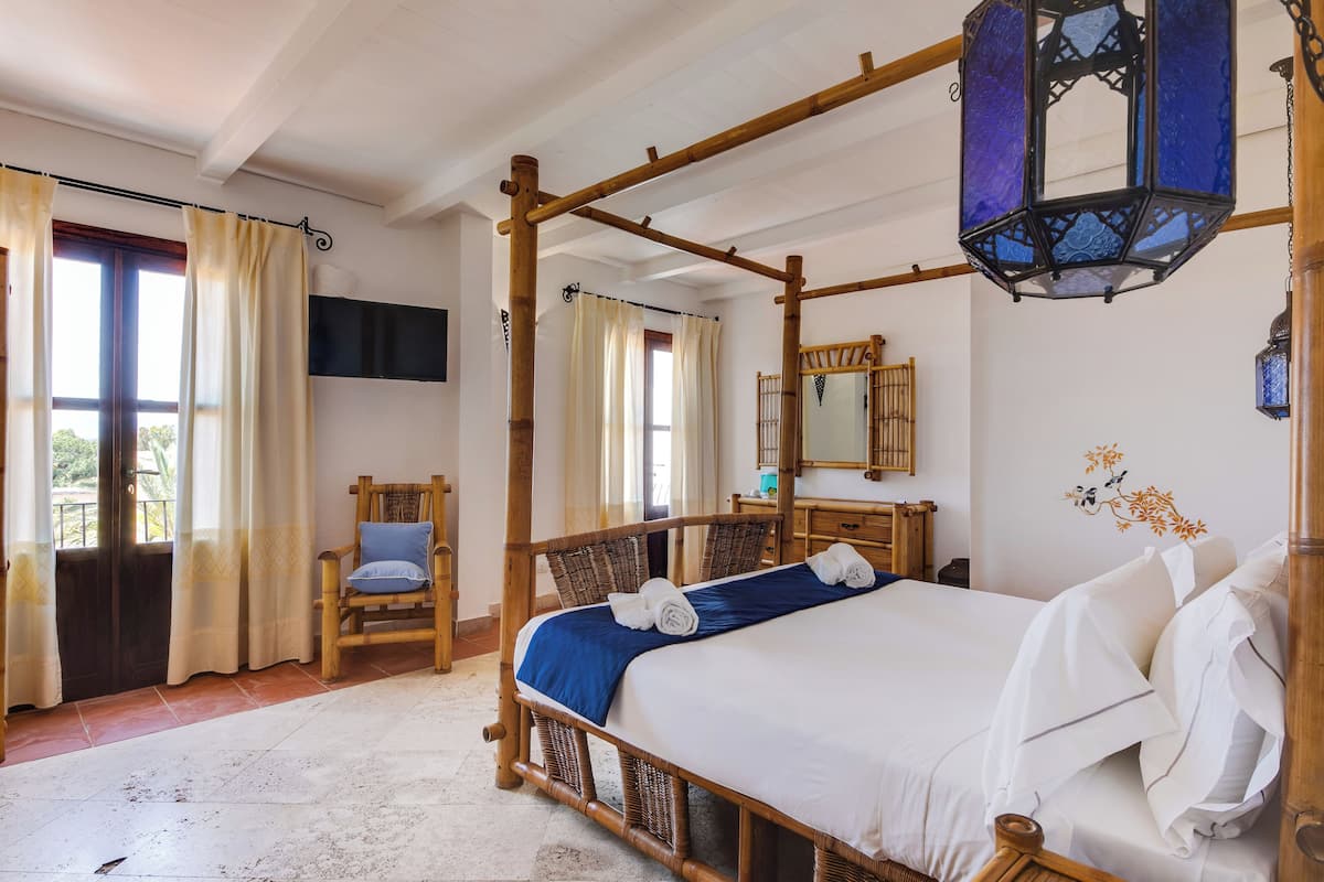 Ein Zimmer mit einem Himmelbett, einem Holzstuhl, einem Nachttisch und einem großen Spiegel.
