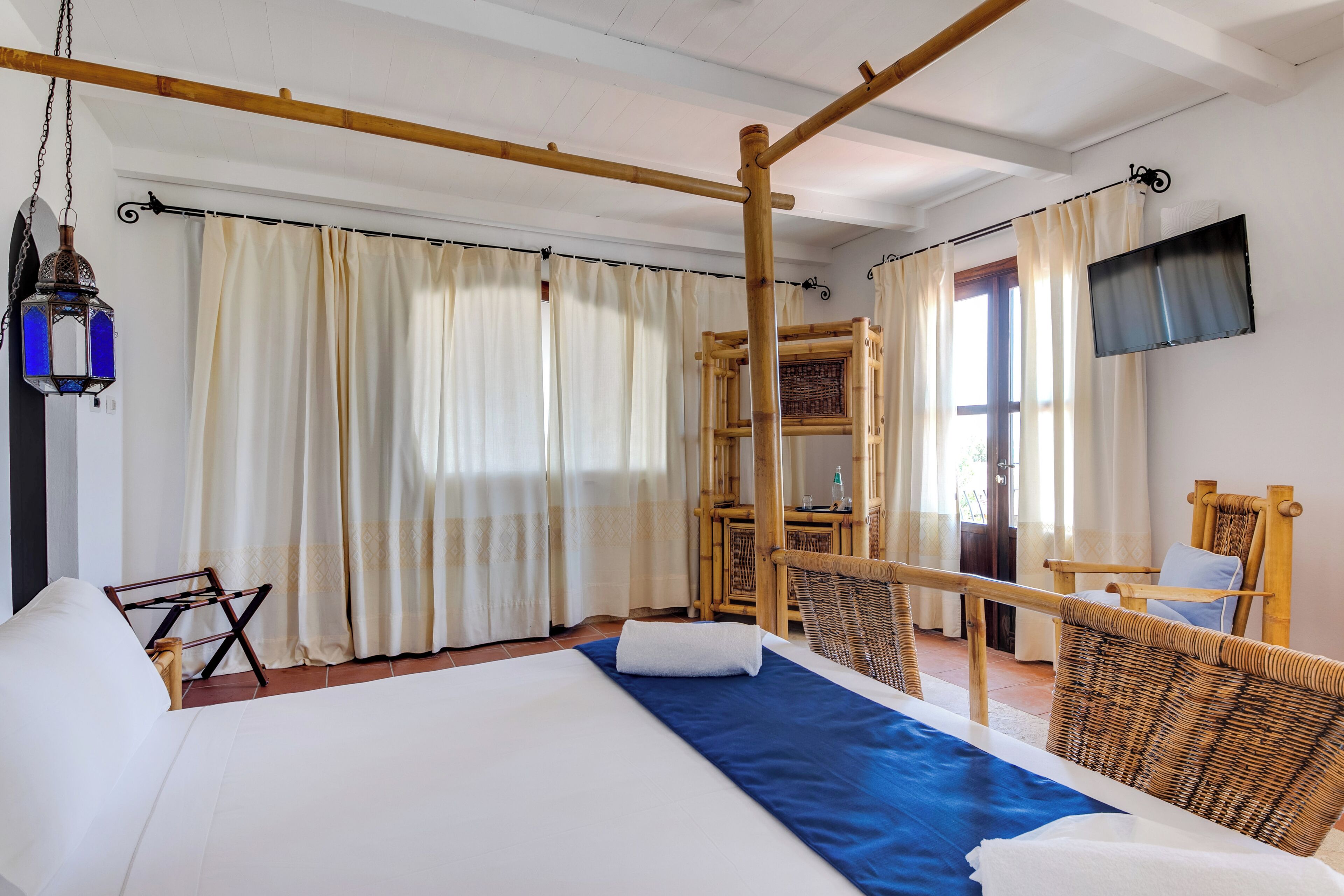 Une chambre d’hôtel avec un lit, une télévision, une chaise en bois et une fenêtre avec des rideaux.