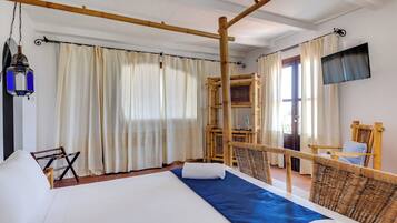 Una habitación de hotel con una cama, televisor, una silla de madera y una ventana con cortinas.