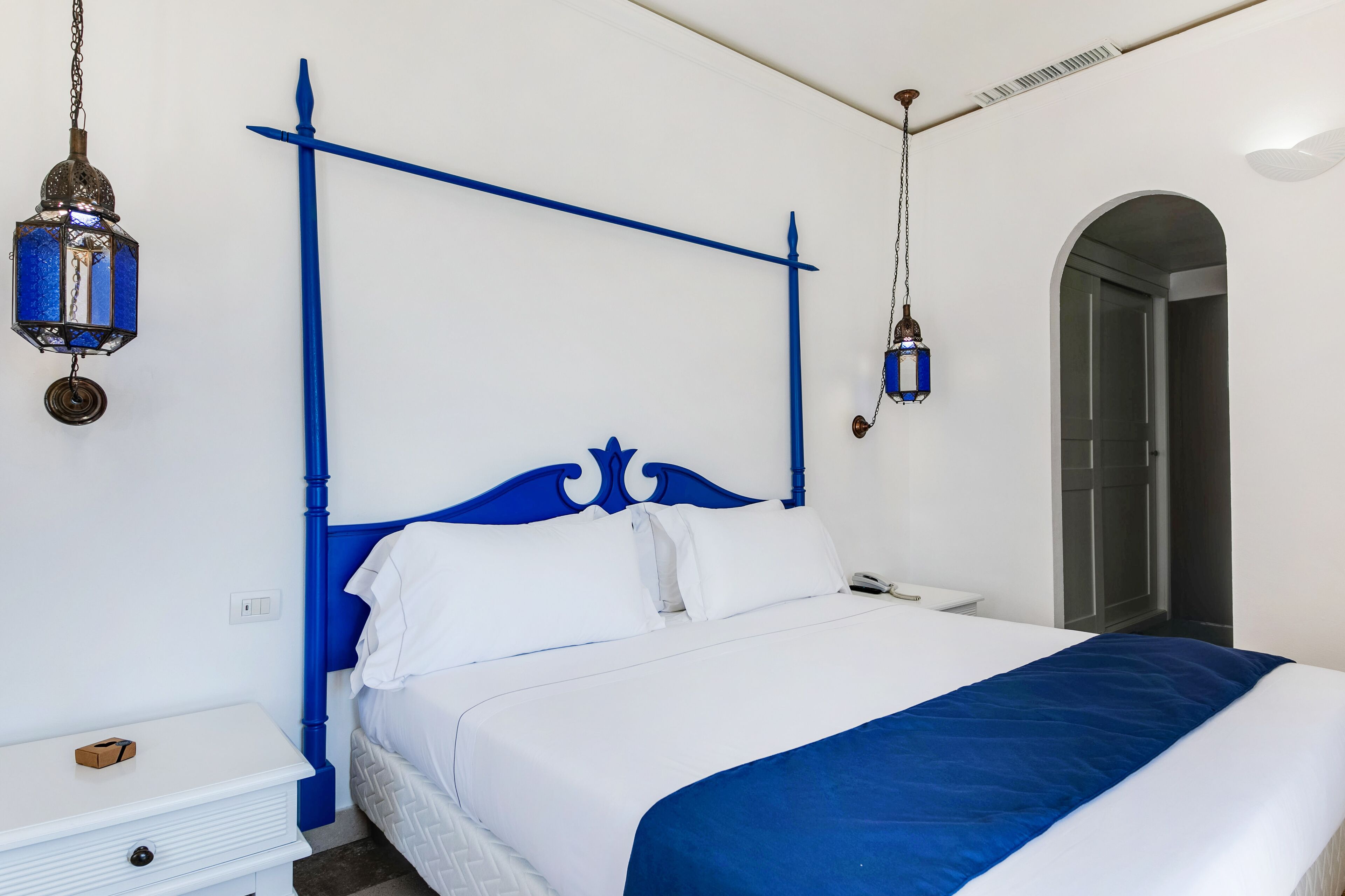 A bedroom with a white bed, blue headboard, and white walls.