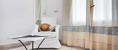 Una habitación con una cama, una mesa con un libro abierto, un sombrero y una ventana con cortinas.