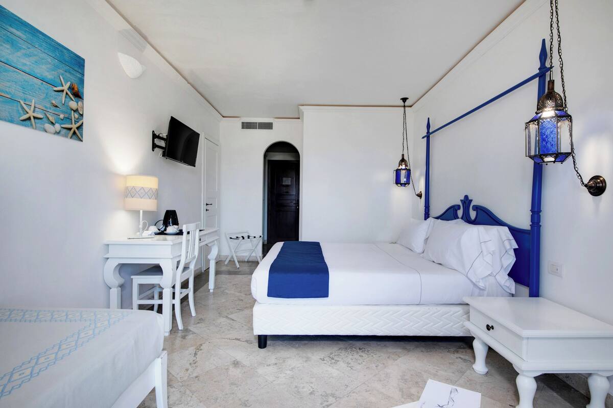 Ein Hotelzimmer mit einem Bett, einem Schreibtisch, einem Sessel, einem Fernseher und einer blauen Wanddekoration.