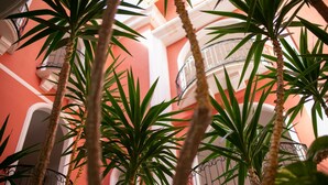 Un exuberante jardín interior con plantas altas y un balcón con barandilla de hierro forjado.