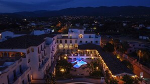 Un hotel con piscina, varios balcones y vistas al pueblo al atardecer.