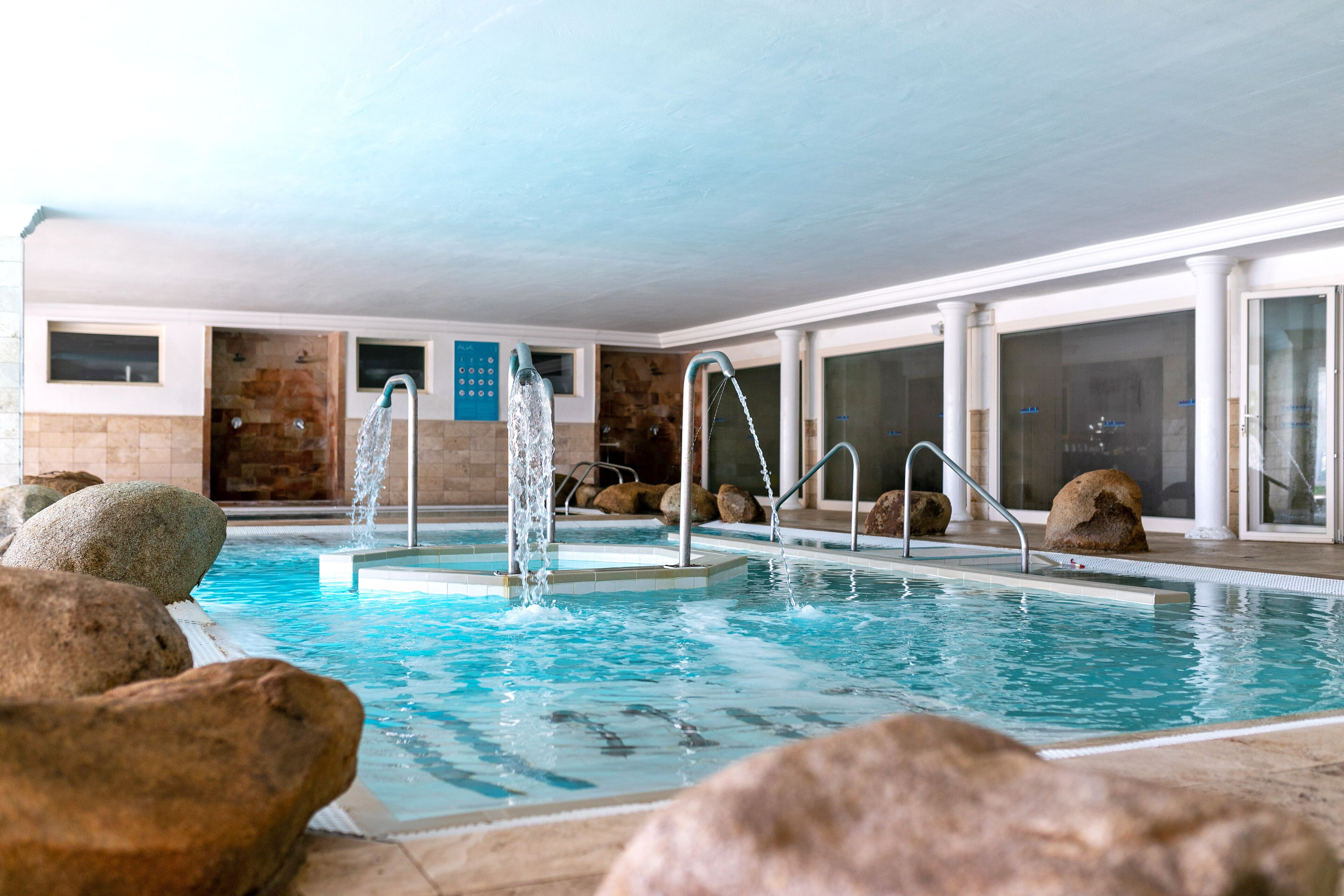 An indoor swimming pool with multiple water jets, surrounded by large rocks and stone walls.