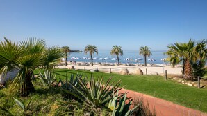 Vista de playa con palmeras, sombrillas y cielo despejado.
