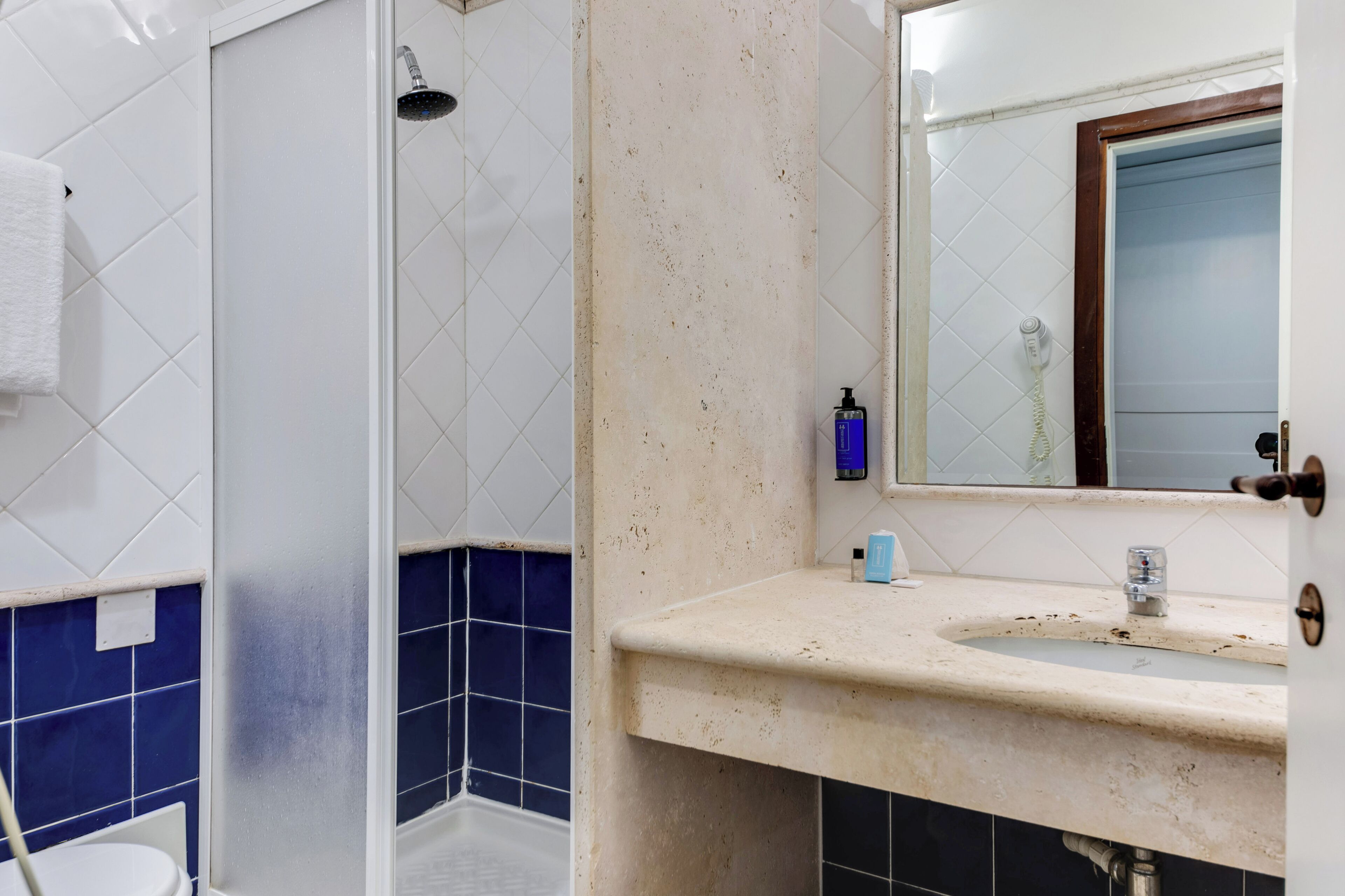 A bathroom with a white sink, blue tiles, a shower, and a mirror with a wooden frame.