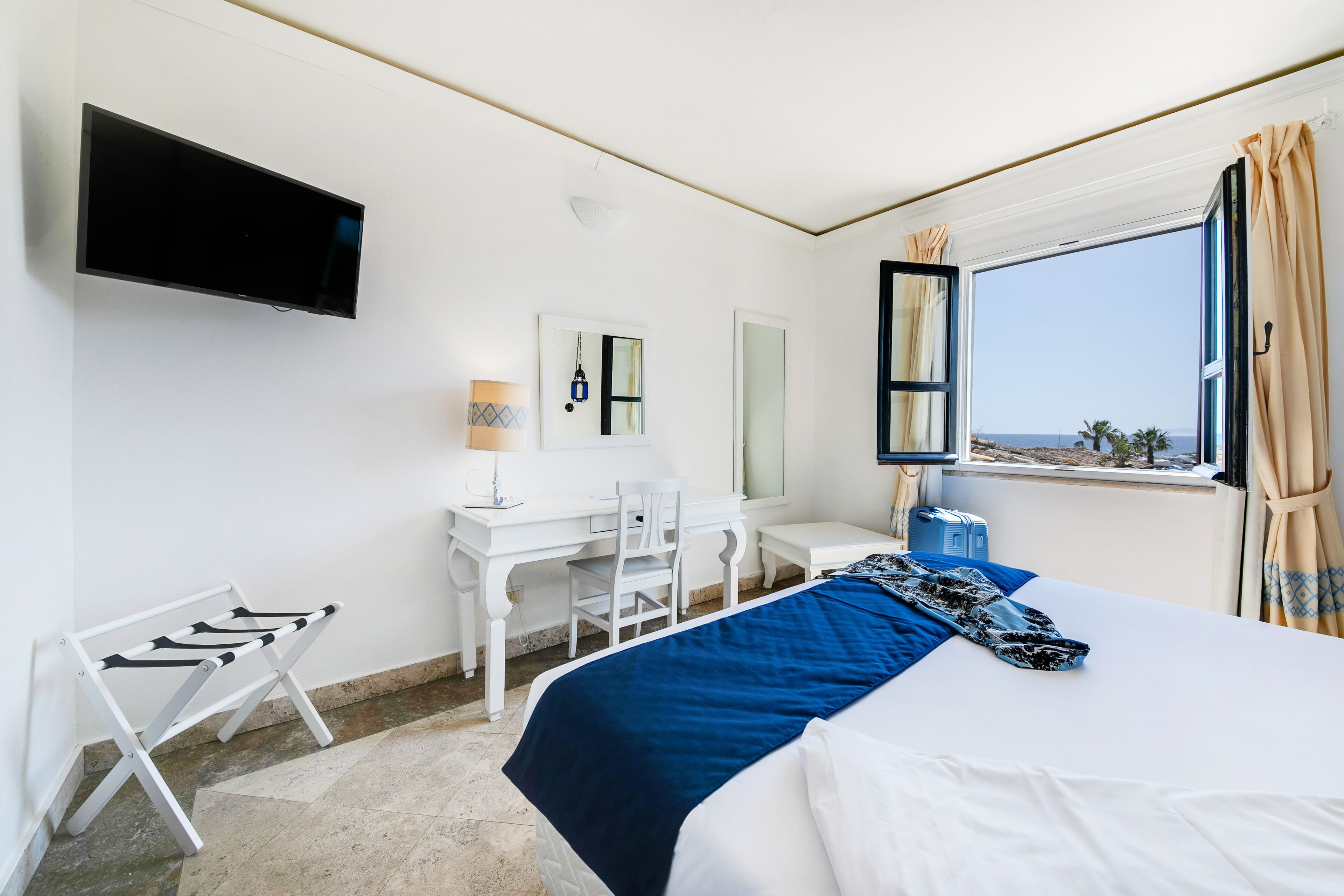 Une chambre d’hôtel avec un lit, un bureau, une chaise, une télévision et une fenêtre avec des rideaux.
