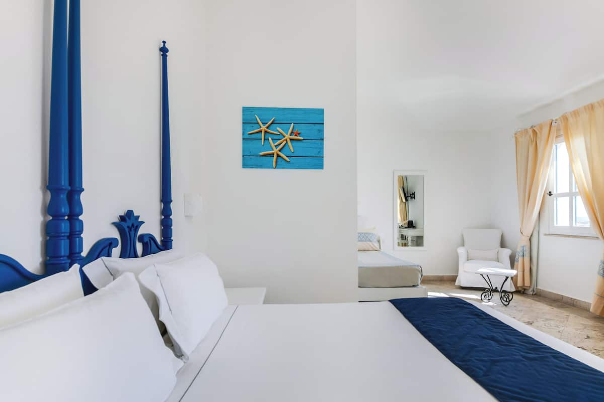 Ein Schlafzimmer mit einem großen Bett, einem Sessel, einem kleinen Tisch und einem Wandbild.