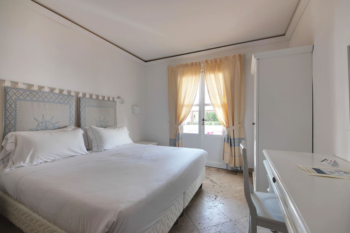 Ein Hotelzimmer mit einem großen Bett, einem Schreibtisch und einem Fenster mit Vorhängen.