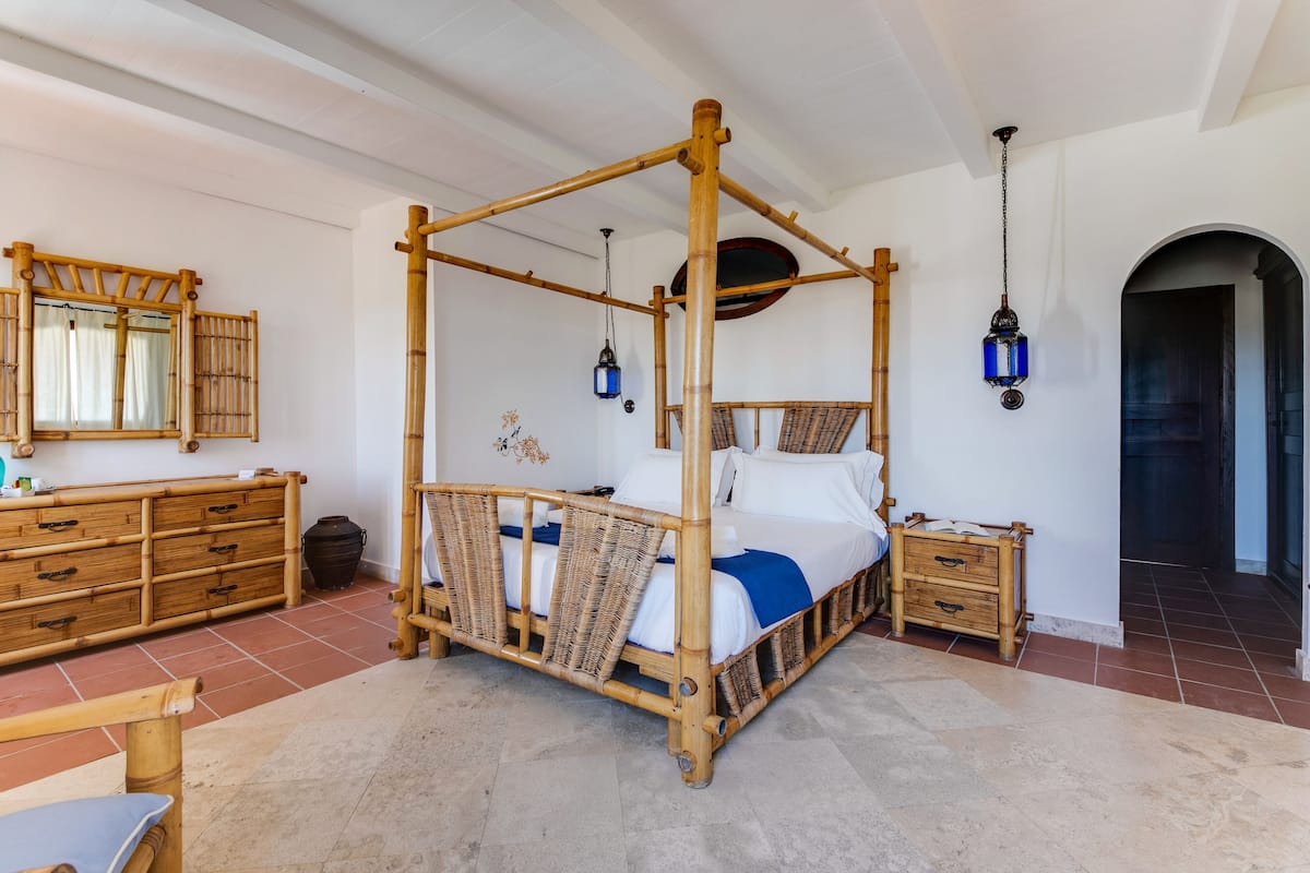 Ein Himmelsbett mit Holzrahmen, ein Nachttisch, ein Spiegel und eine Pendelleuchte.