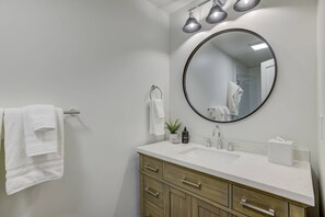 A modern bathroom with a white sink, wooden vanity, and a round mirror.
