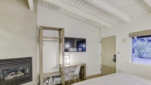 Een slaapkamer met een bed, een bureau met stoel, een televisie, een kledingkast en een open haard.