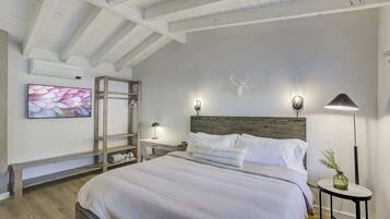 A bedroom with a large bed, a wooden headboard, a bedside table with a lamp, a wall-mounted shelf, and a decorative deer skull.