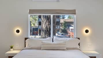 A bedroom with a large window, a bed with white linens, two bedside tables, and wall-mounted lights.