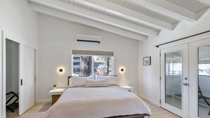 Un dormitorio con una cama grande, una ventana con cortinas, un equipo de aire acondicionado y una puerta corredera de vidrio.