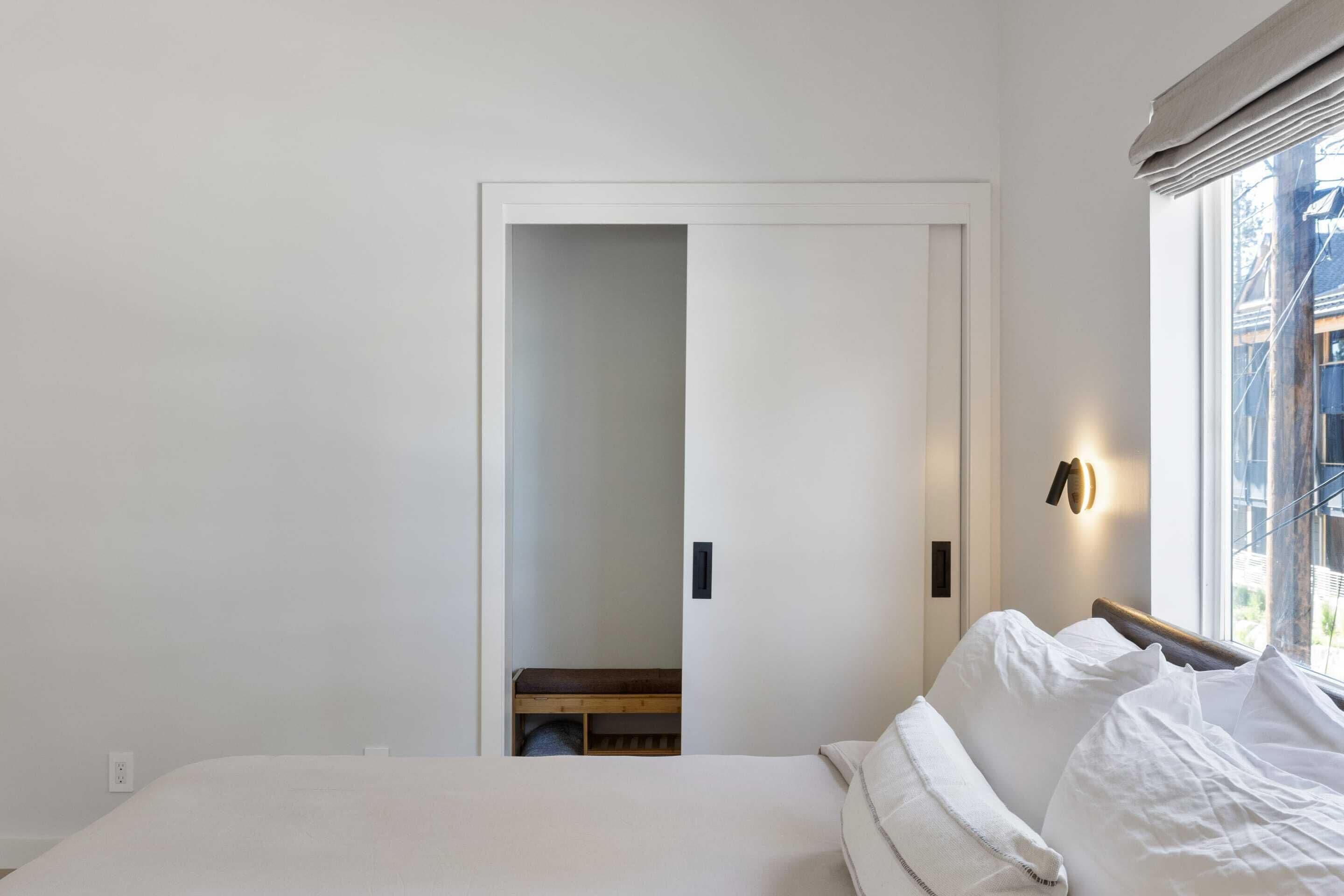 Een slaapkamer met een bed, nachtkastje, raam met uitzicht en deur naar een andere kamer.