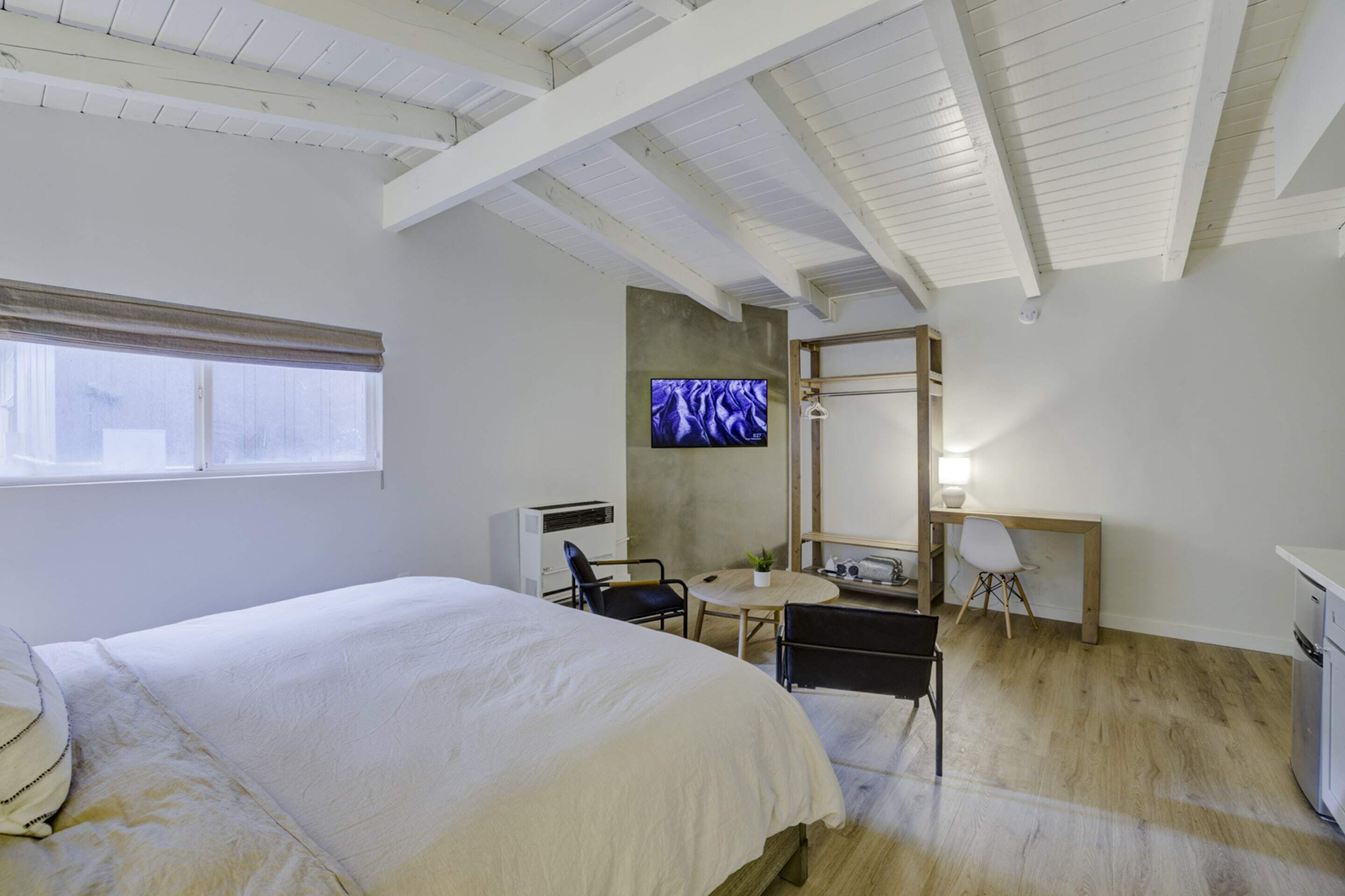 A bedroom with a bed, a desk, a chair, a television, and a window.