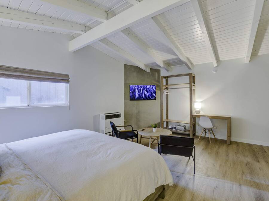 A bedroom with a bed, a desk, a chair, a television, and a window.