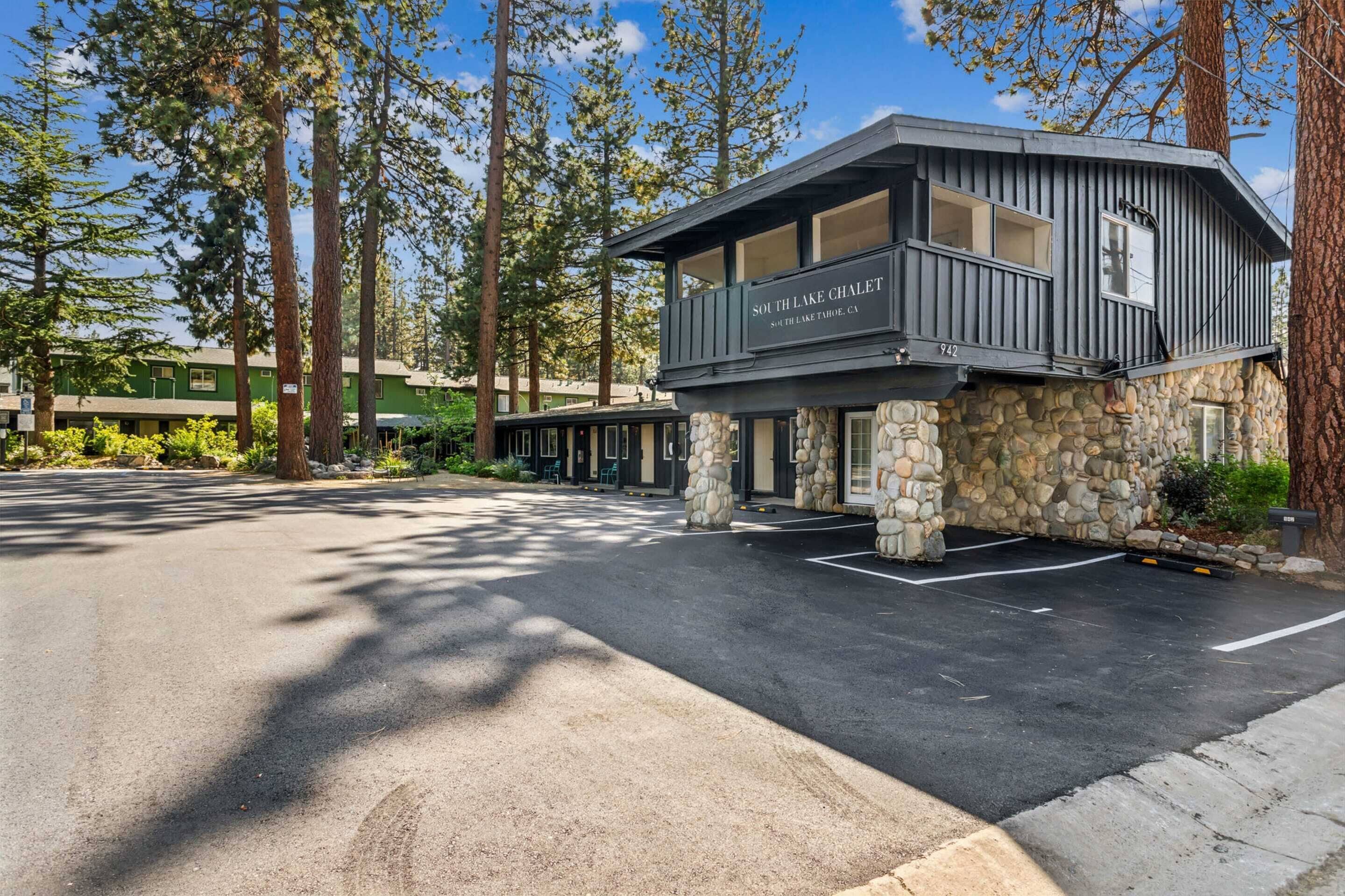Una cabaña con base de piedra y nivel superior de madera, llamada 'South Lake Chalet', ubicada en una zona boscosa con estacionamiento.