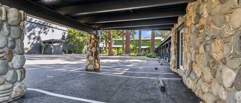 A covered parking area with stone walls, a clear path, and a building in the background.
