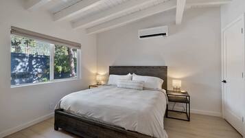 A bedroom with a large bed, two bedside tables with lamps, a window with blinds, and a door.