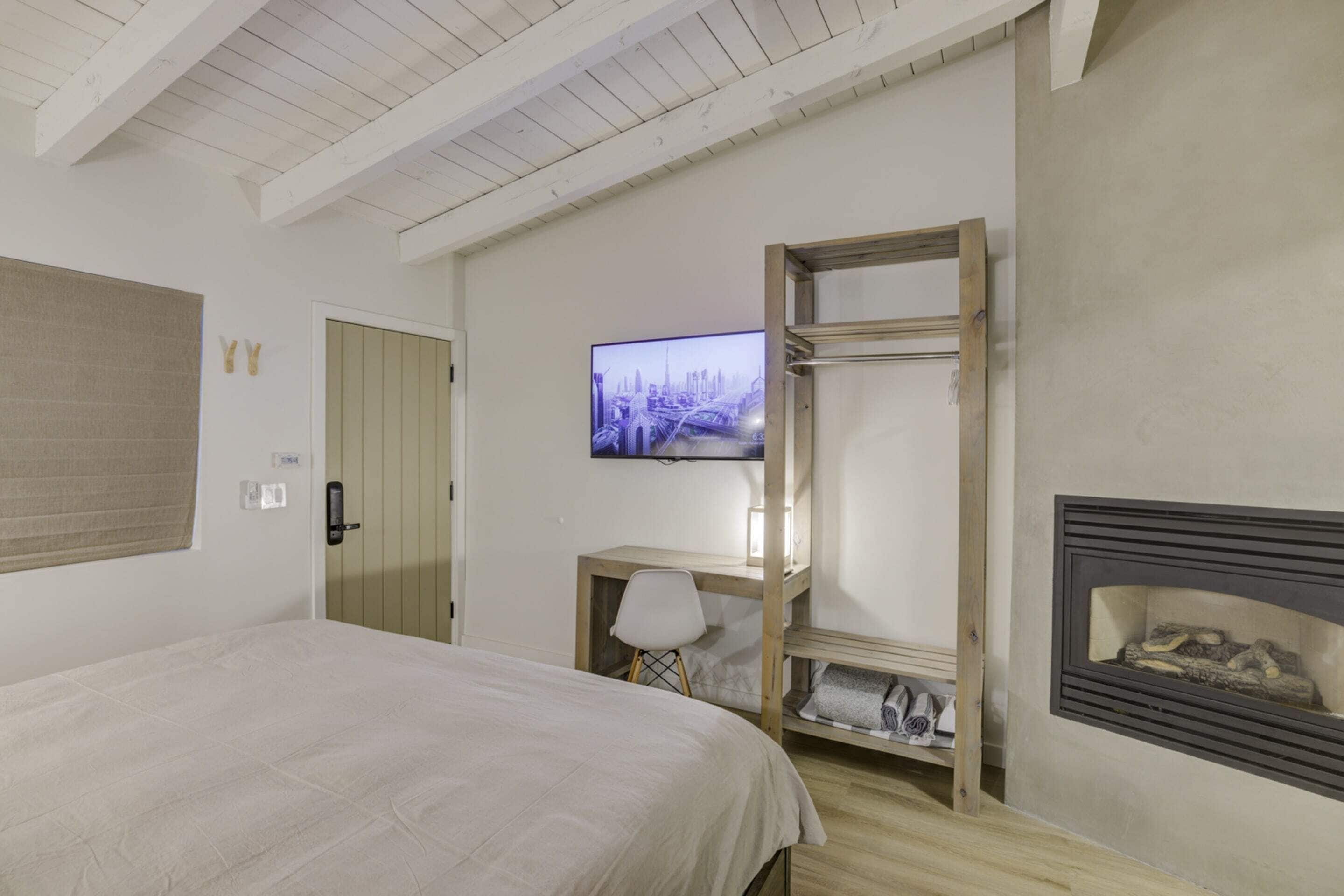 A bedroom with a bed, a desk, a TV, and a fireplace.