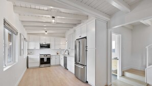 Una cocina amplia con muebles blancos, electrodomésticos de acero inoxidable y piso de madera.