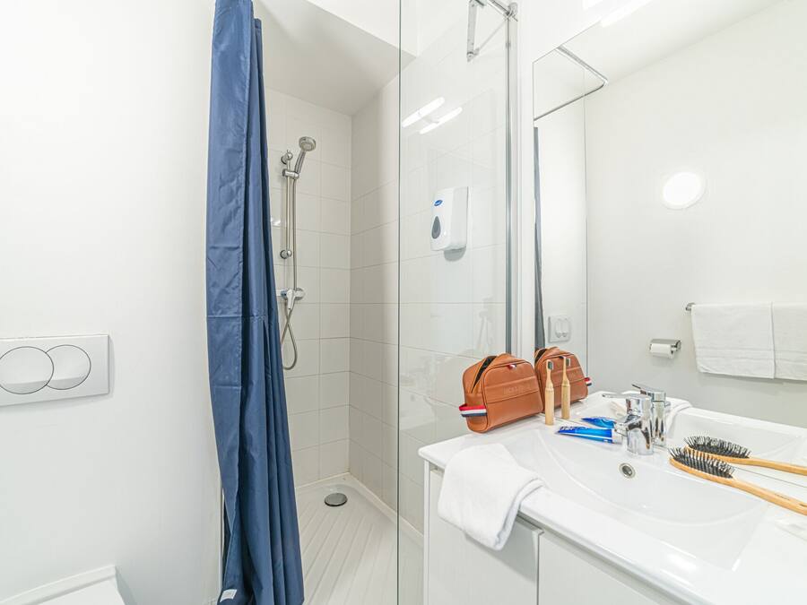 Un baño moderno con cabina de ducha de vidrio, un lavabo blanco con artículos de aseo y un espejo.